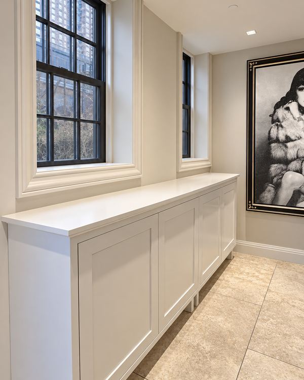 Run of white painted shaker cabinets beneath windows in a long hallway