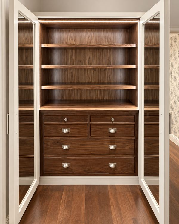 Walnut wardrobe interior with lit shelves and a bank of drawers behind white glass-panel doors