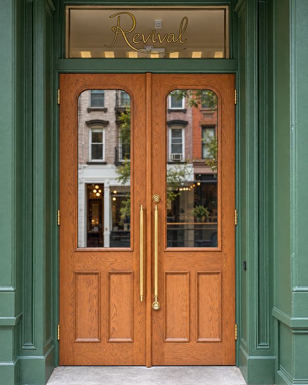 Oak double entry doors with arched glass and brass pulls in a green painted restaurant storefront