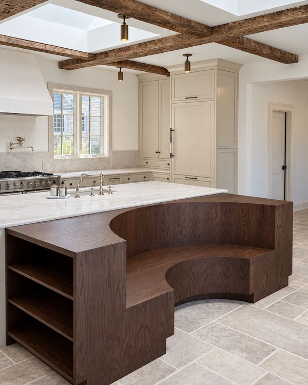 Walnut kitchen island with a built-in curved banquette and open end shelves, under reclaimed beams and skylights